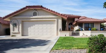 Suburban house with two-car garage, driveway, front lawn, and red tile roof under a blue sky